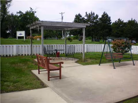 Outdoor seating area with benches, swing, and a pergola at a nursing facility.