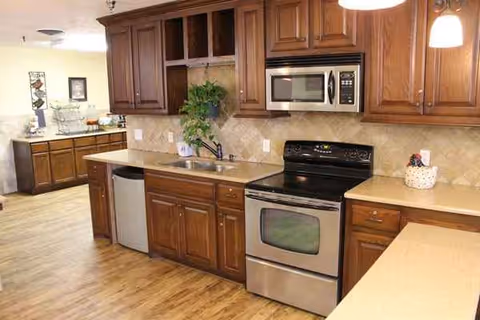 Wooden cabinets and stainless steel appliances line a spacious senior living facility kitchen.