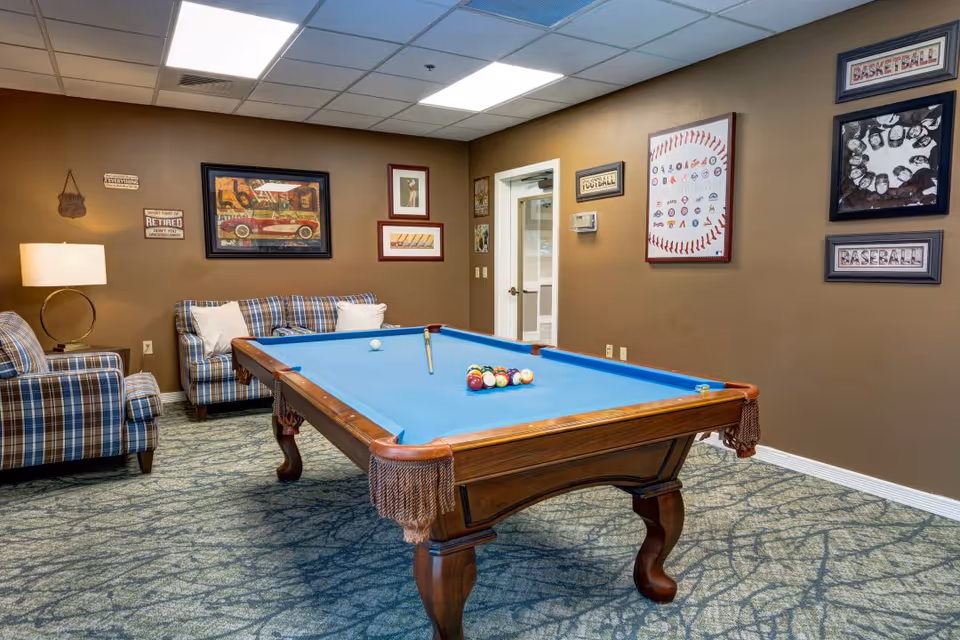 Indoor game room with a pool table, plaid couches, and sports-themed wall art.