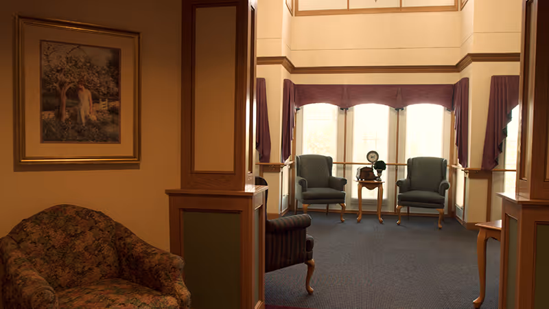 A cozy sitting area in an assisted living facility with floral patterned armchairs, two blue upholstered chairs near large windows with purple valances, a small wooden table with a vintage clock and a decorative item, and a framed painting on the wall.