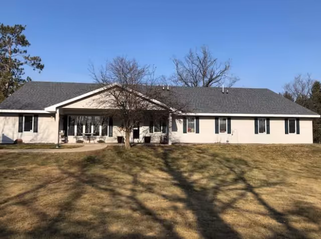 Single-story building with a gray roof and light-colored exterior walls, surrounded by a grassy area with leafless trees under a clear blue sky.