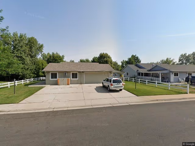 Single-story house with a wide concrete driveway, a white SUV parked out front, and white fencing on a suburban street.