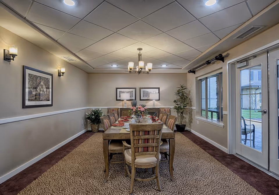Well-lit dining room with a long table set for a meal, chandelier overhead, and glass doors to an outdoor patio.