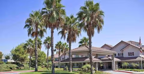 Front exterior view of Holiday Valencia Commons, a senior living facility with palm trees and porte-cochere.