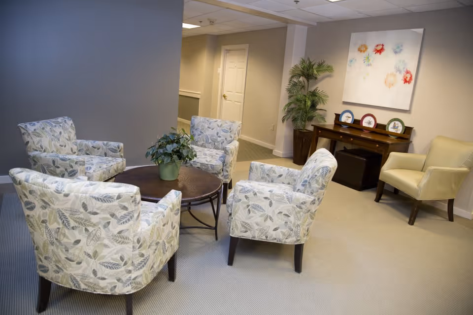 A cozy seating area with four patterned armchairs around a round coffee table, a potted plant, and a console table with decorative plates.