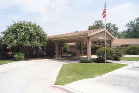 Senior living facility entrance with a covered driveway, flagpole, and manicured landscaping.