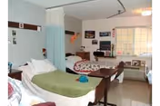 Shared nursing home bedroom with two hospital-style beds, a privacy curtain, window and bedside tables.