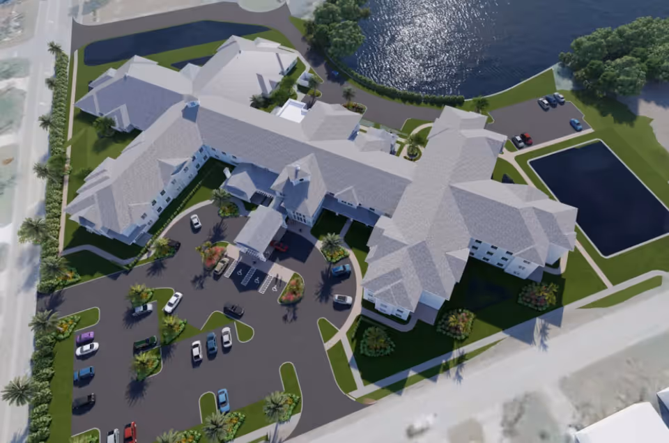 Aerial rendering of a multi-wing senior living building with a circular drive, parking lot, landscaped grounds and a pond.