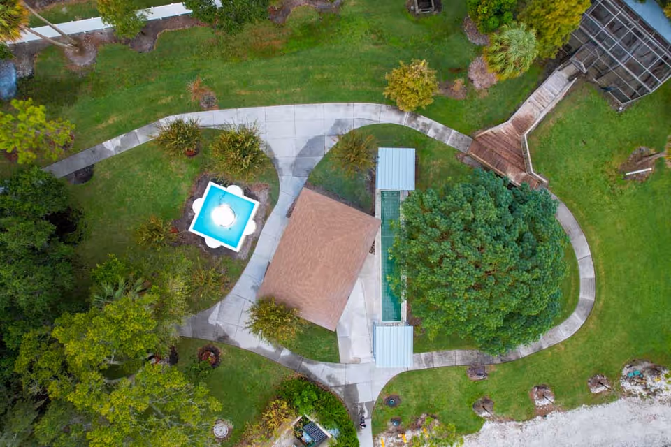 Aerial view of landscaped outdoor grounds with winding walkways, a small pavilion, fountain, and surrounding trees.
