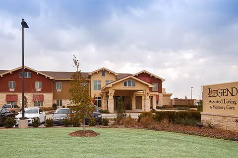Front view of Legend of Fort Worth senior living facility with entrance, sign, and parked cars.