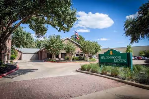 Exterior view of a senior living facility with a driveway and entrance sign.