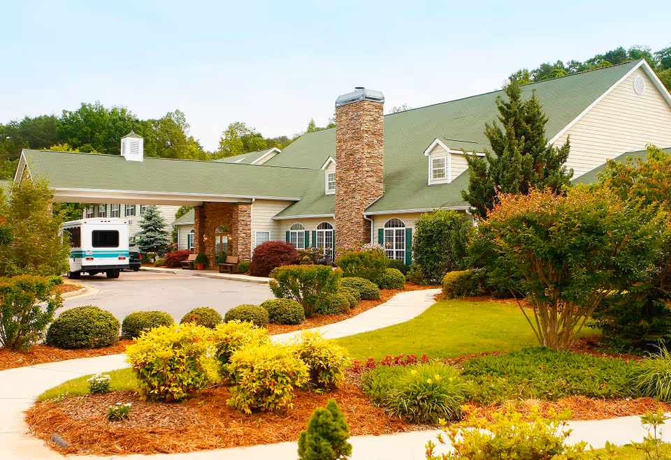Landscaped front entrance of a senior living facility with a covered porte-cochère and a parked shuttle van.
