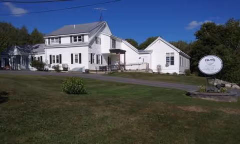 White, multi-wing senior living facility exterior with a manicured lawn and a street sign.