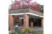 Brick entrance with a covered portico at Premier at Perry Village, surrounded by foliage.