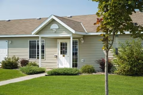 Front exterior of a beige townhome-style senior living building with a green lawn.