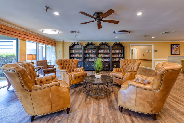 Cozy lounge with five tufted leather armchairs arranged around a round coffee table, bookcases and large windows.
