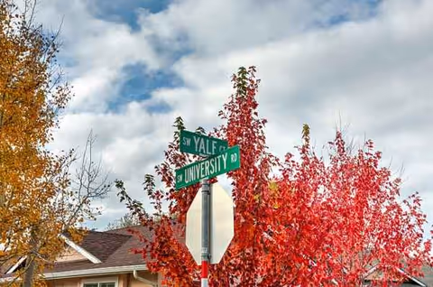 Intersection street signs near a home with red autumn trees and cloudy sky