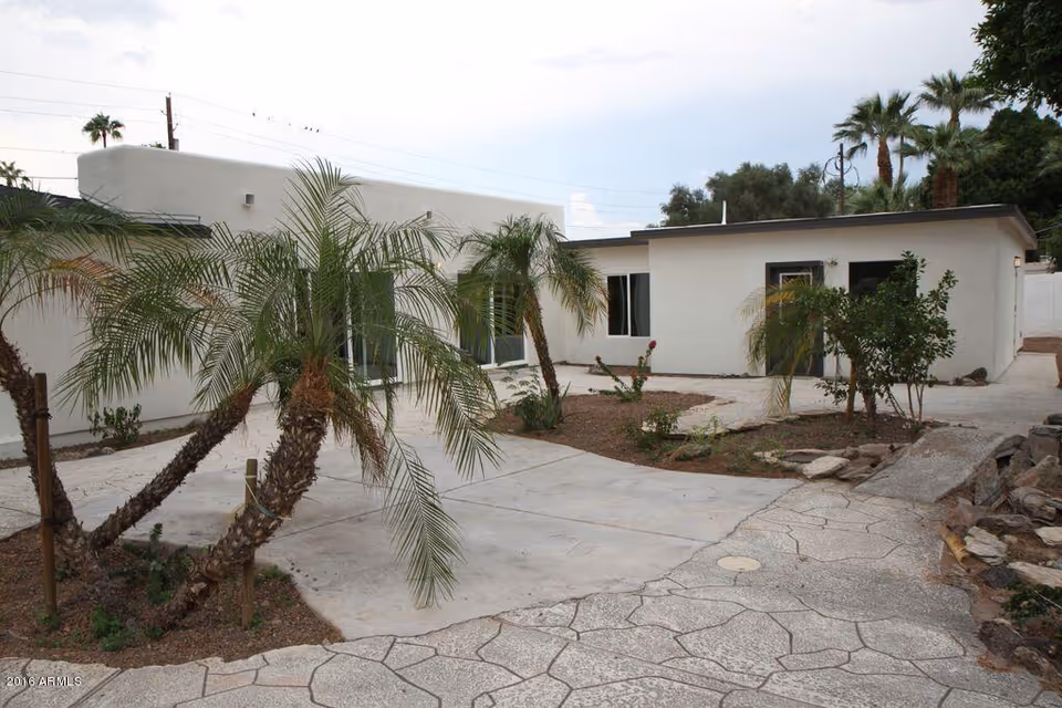Single-story white building with a paved courtyard and palm trees in front.