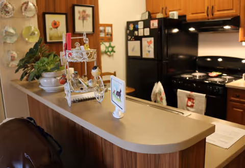A cozy kitchen area with wooden cabinets, a black refrigerator decorated with children's drawings, a black stove with a towel hanging on the handle, and a countertop with decorative items including a small white metal stand, a potted plant, and a small framed picture.