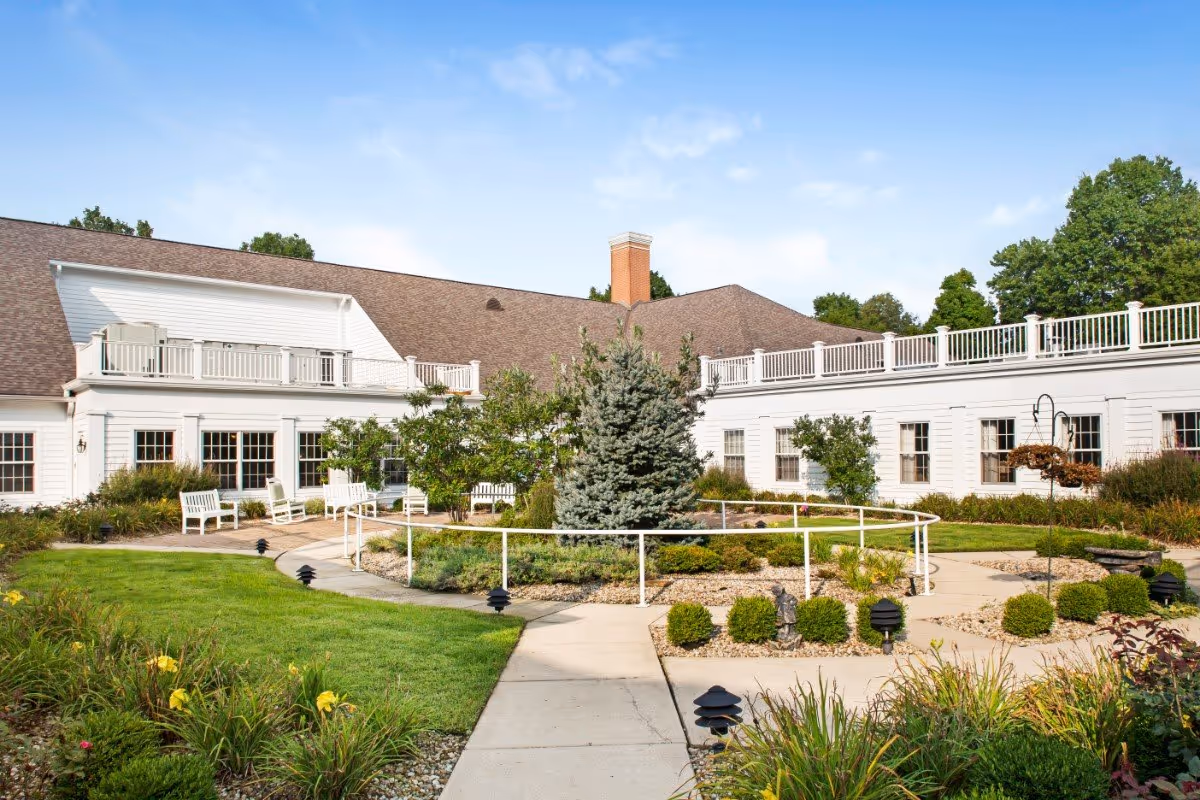 A landscaped courtyard with a paved walkway, raised garden beds, benches, and a white two-story building with balconies.