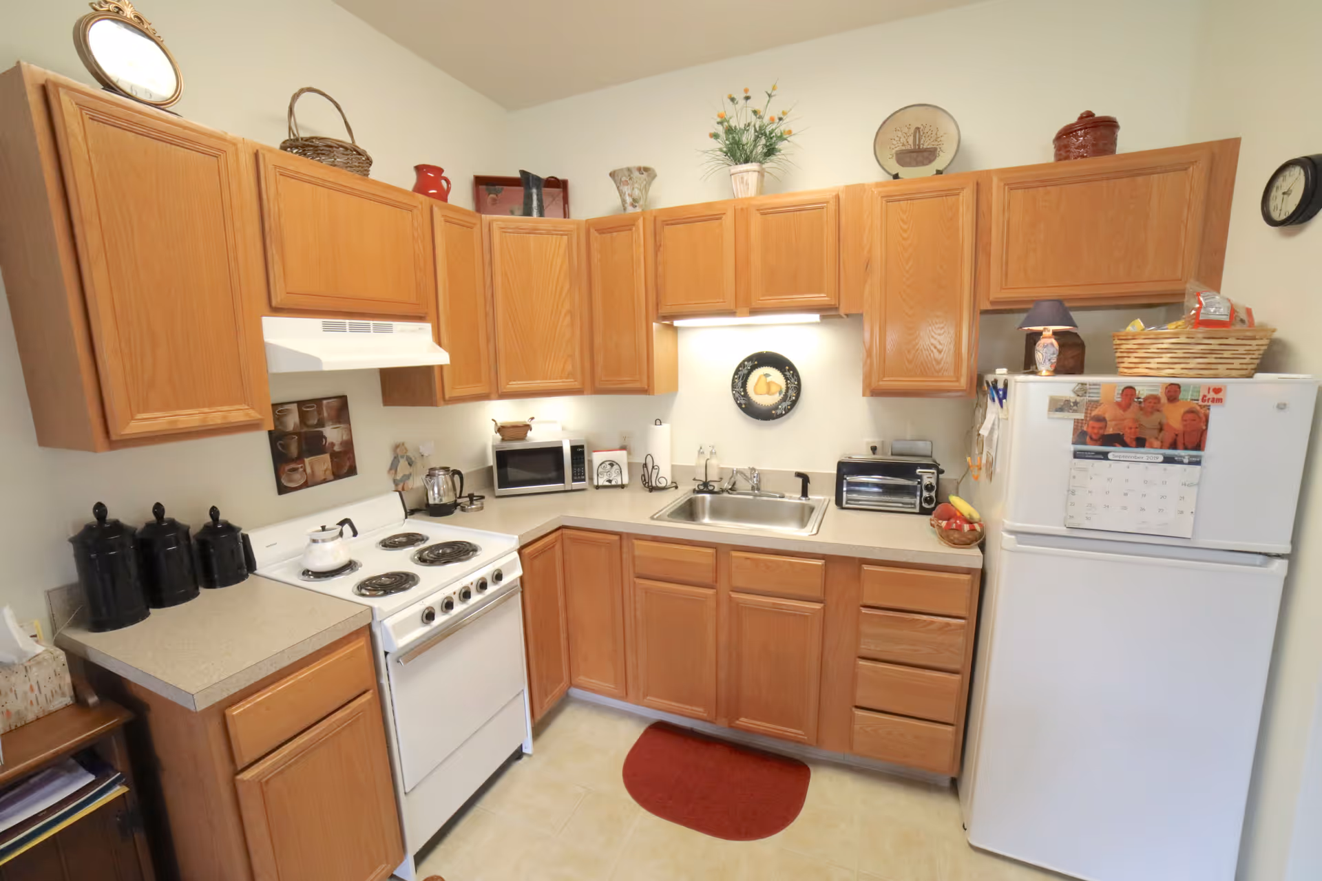 Small kitchen with oak cabinets, a white stove and refrigerator, a double sink, countertop appliances, and decorative items.