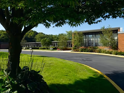 Atria Huntington exterior view showing a brick building, driveway, trees, and landscaped lawn.