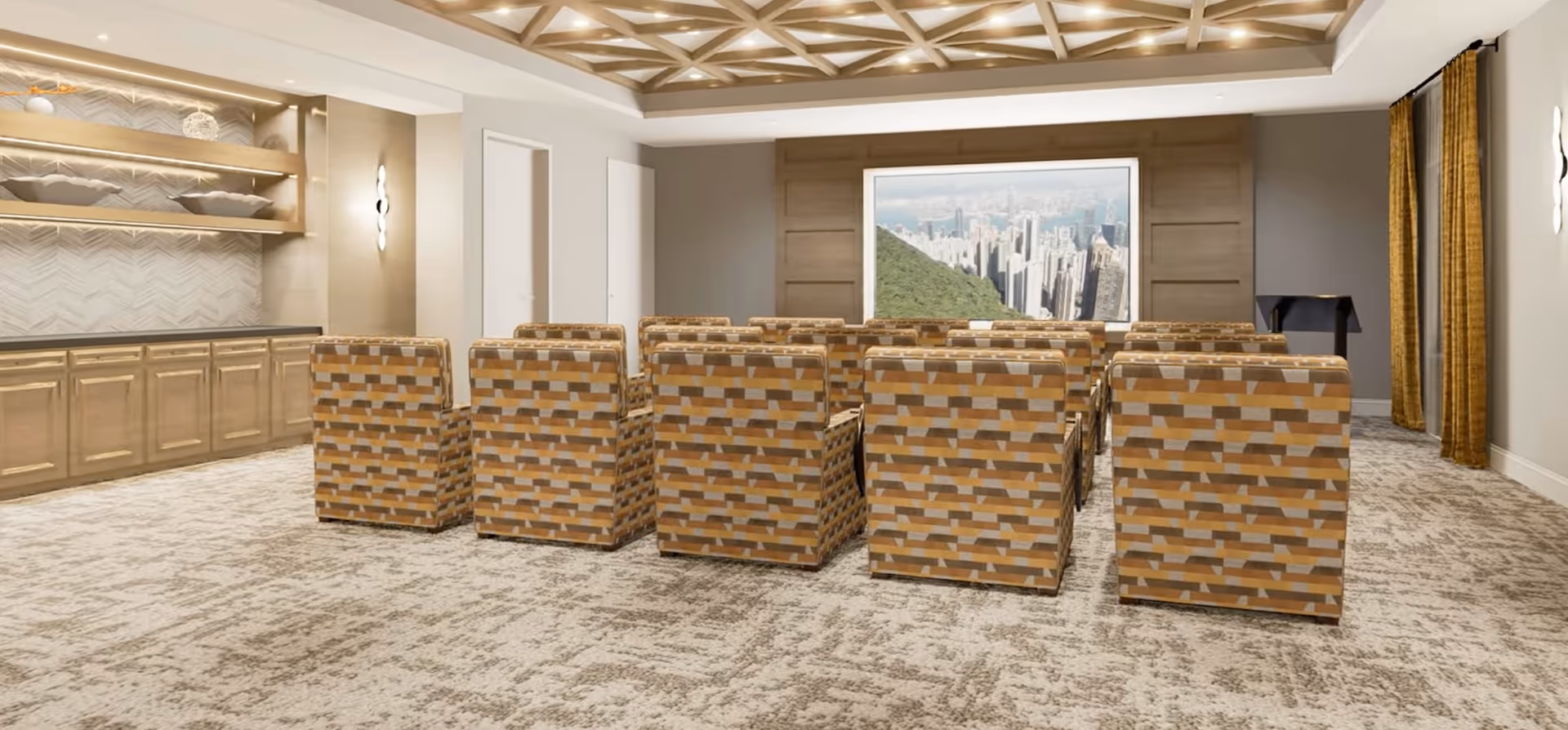 A small theater room with multiple rows of patterned armchairs facing a large screen displaying a cityscape. The room features a decorative coffered ceiling with recessed lighting, a carpeted floor, wooden cabinetry with shelves on the left wall, and gold curtains on the right side.