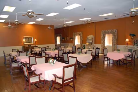 A spacious dining room with pink tablecloths and wooden chairs against warm orange walls.