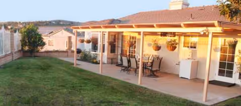 Outdoor covered patio with table, chairs, hanging planters, and grassy yard at Allison's Home Care.