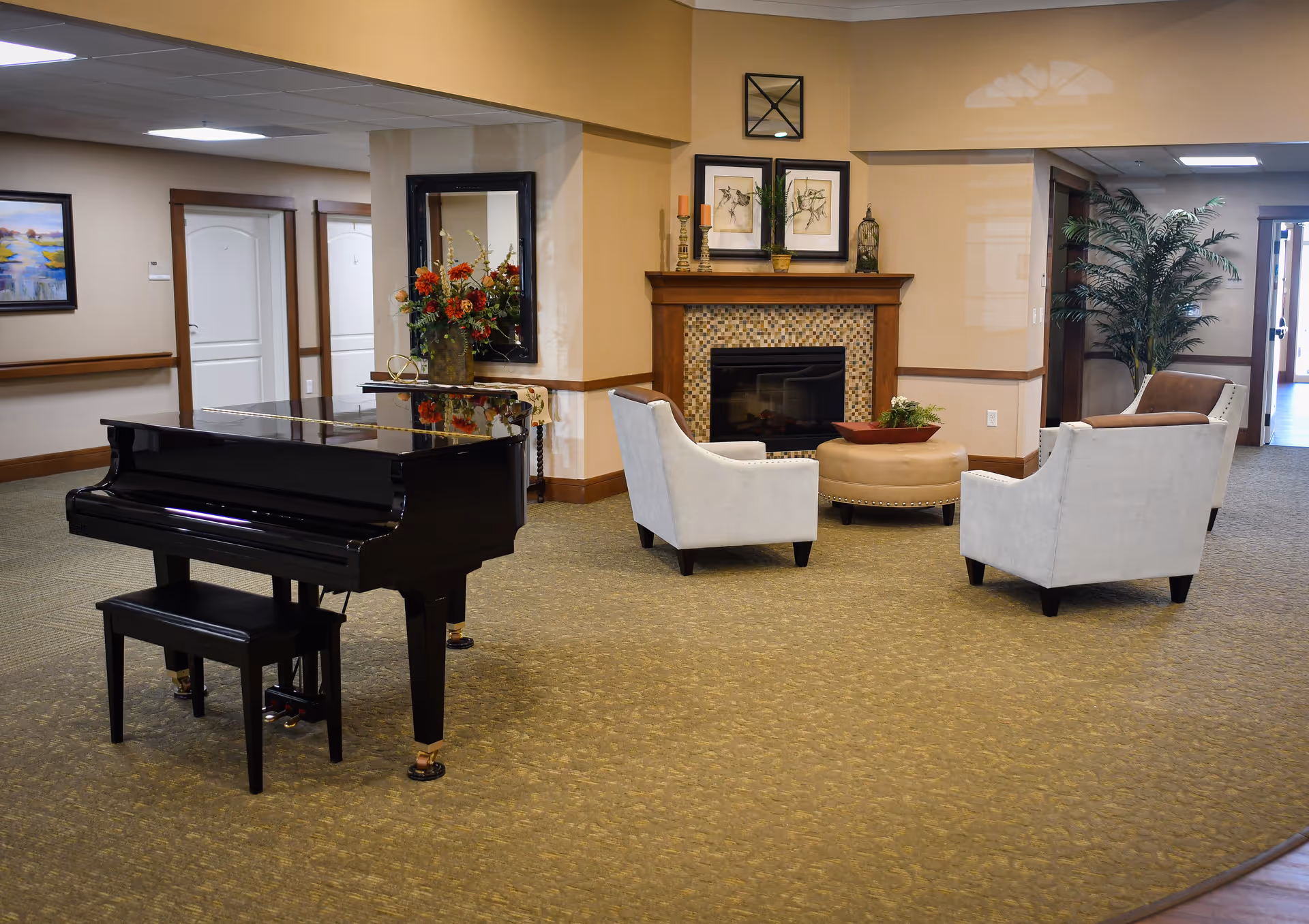 Spacious senior living common area with a black grand piano, a seating group around a fireplace, and decorative plants and artwork.
