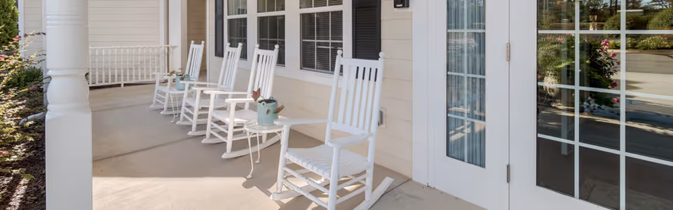 Front porch with several white rocking chairs lined up beside a glass-paned door.