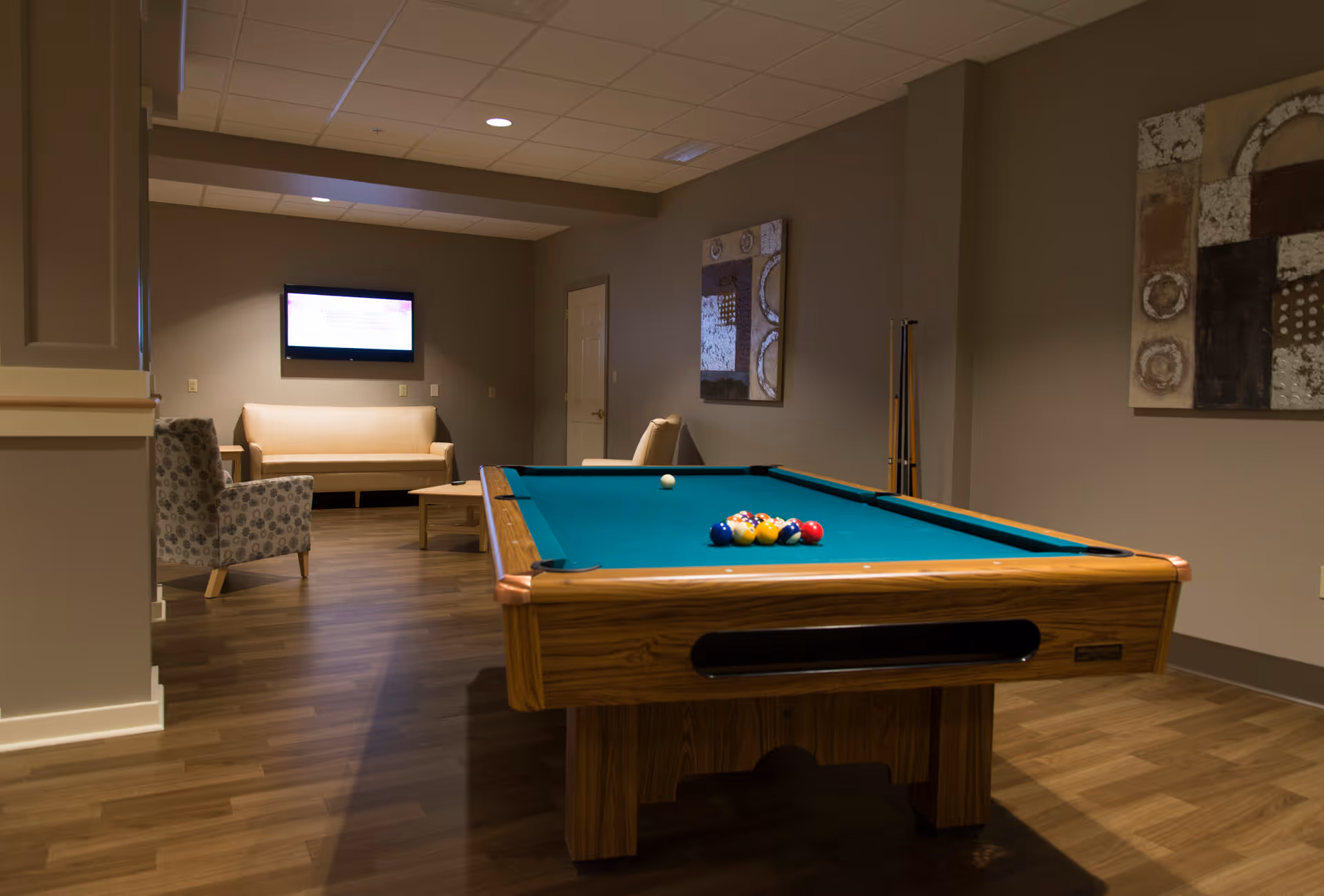 A pool table in a cozy lounge area with seating, wall art, and a mounted TV.