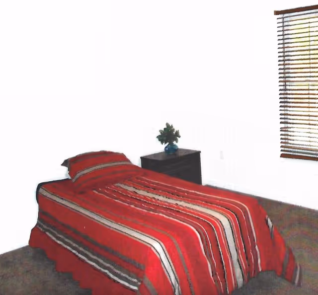 A simple bedroom with a striped red bedspread, nightstand, small plant, and window blinds.