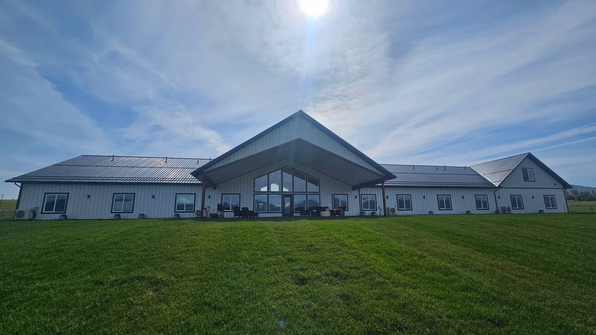 Wide exterior view of a single-story senior living facility building with a large green lawn in front, under a partly cloudy blue sky.