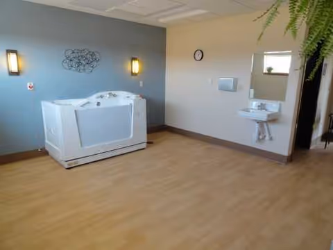 Spacious interior room with a standalone spa tub, wall-mounted sink, and hanging greenery.