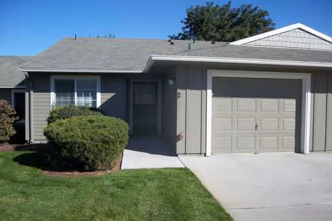 A single-story gray building with a front door and attached garage.