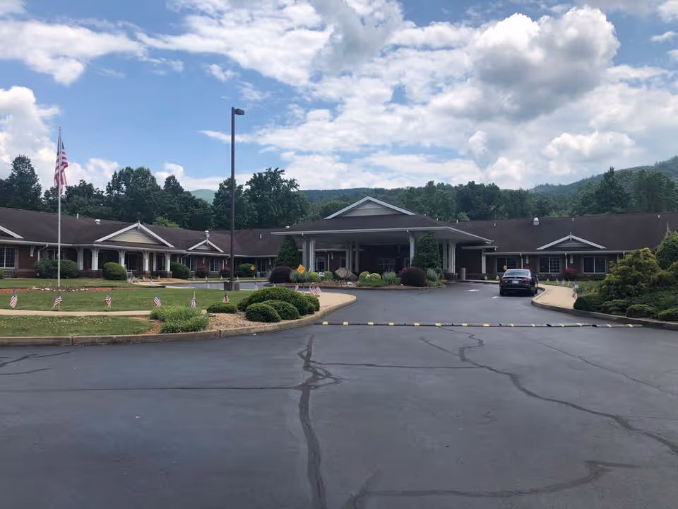 Single-story brick building with a covered entrance, landscaped driveway, flagpole and a parked car under a partly cloudy sky.
