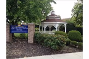 Outdoor view of the Church of God Home sign next to a white gazebo surrounded by green bushes and trees.
