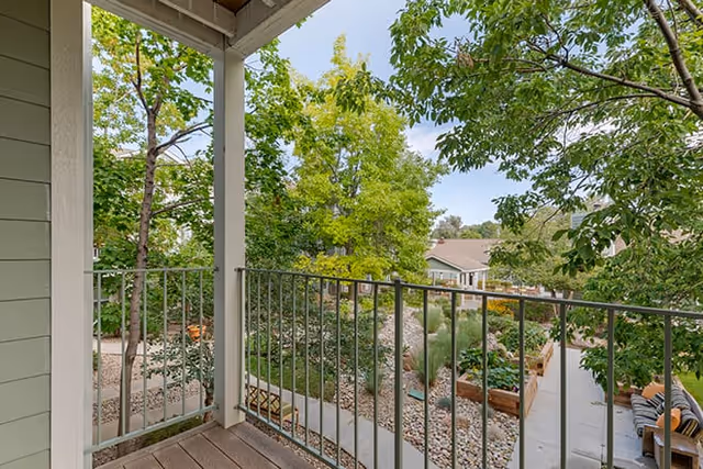 View from a balcony overlooking a landscaped courtyard with trees, raised garden beds, walkways, and outdoor seating.