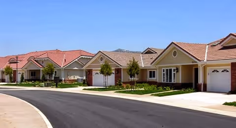 Row of single-story houses with garages along a curved paved street in a residential community.