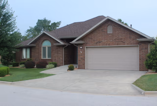 Brick single-story house with an attached two-car garage, driveway, and landscaped front lawn.