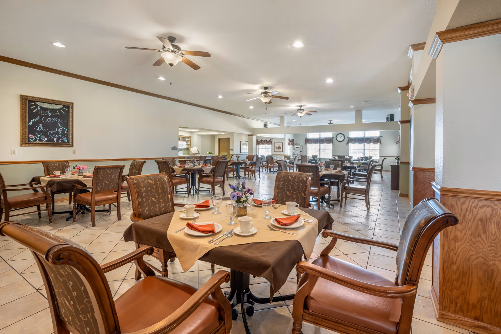 Spacious dining room with multiple set tables and chairs, ceiling fans, and place settings arranged for a meal.