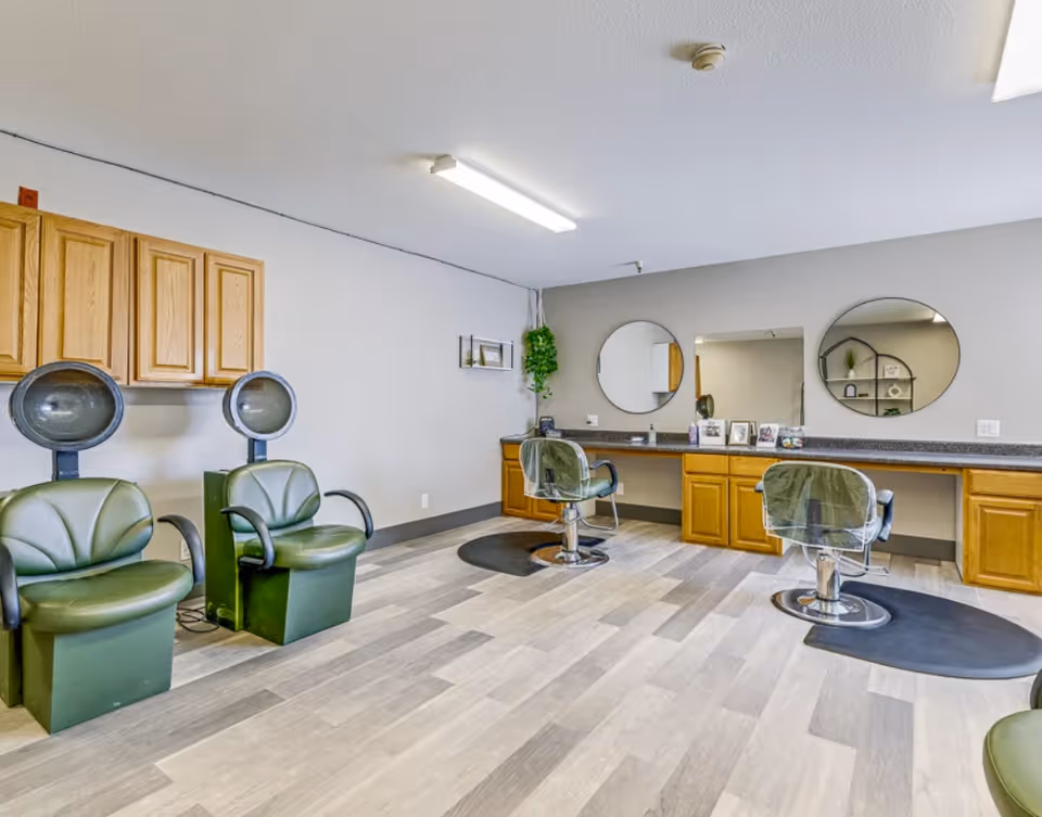 Interior salon area with styling chairs, hooded hair dryers, round mirrors, and wooden cabinets.