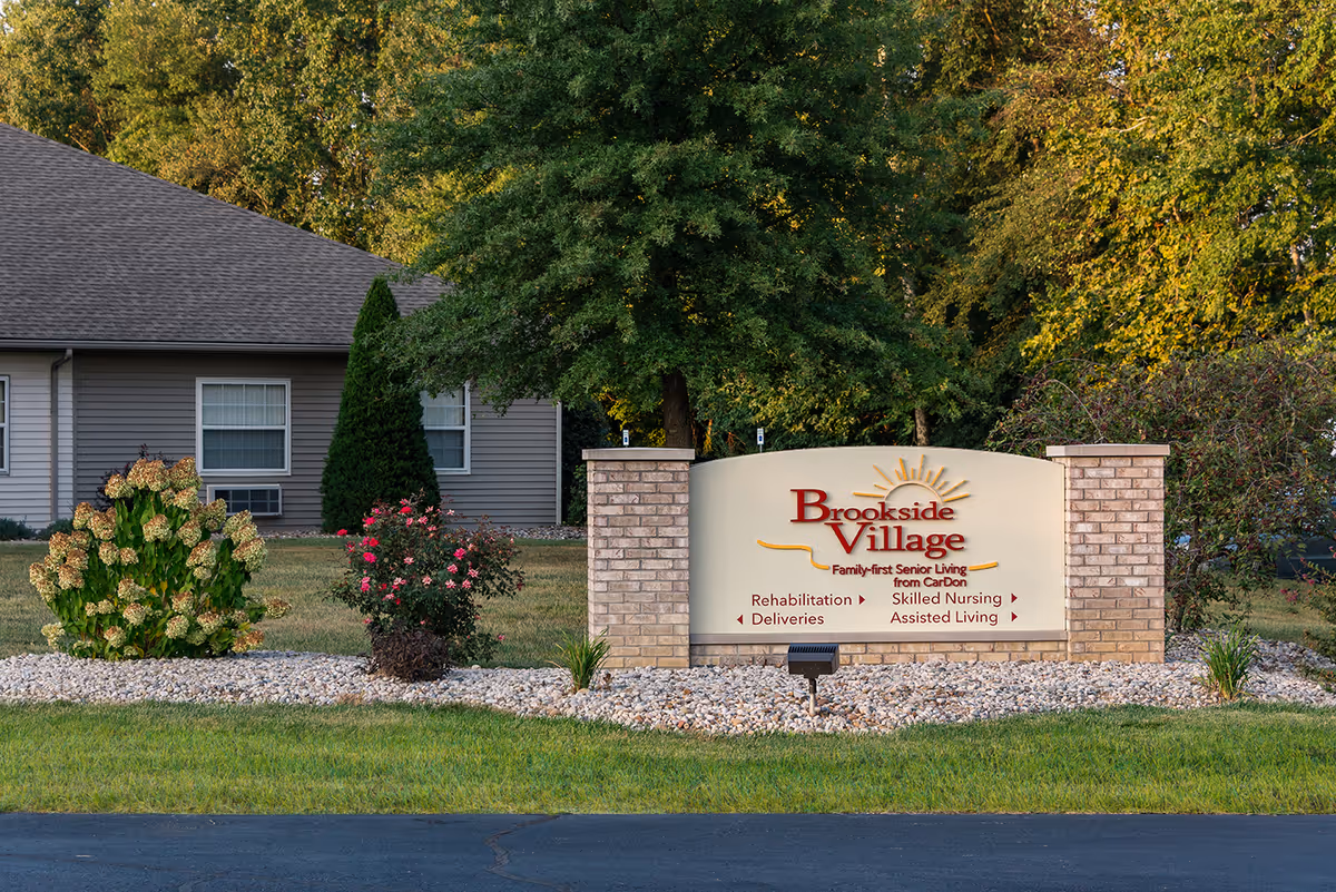 Stone-and-brick entrance sign for Brookside Village senior living in front of a single-story building and landscaped lawn