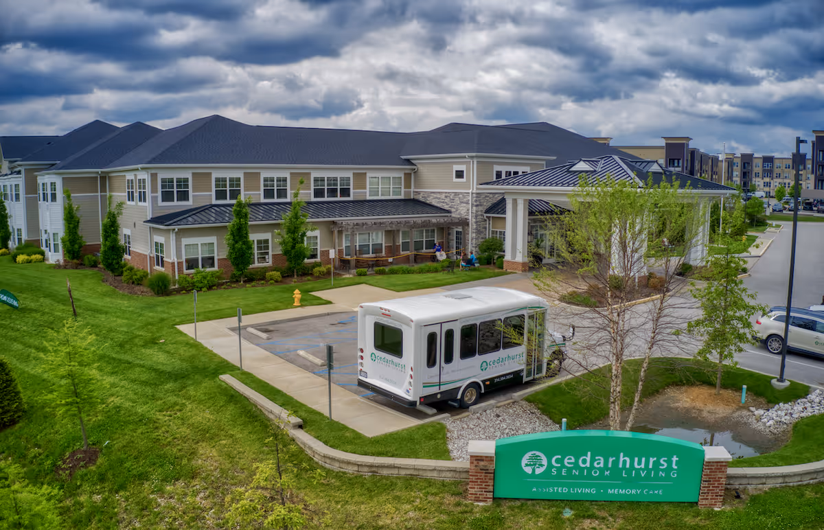 Exterior view of Cedarhurst Senior Living building with a shuttle parked near the entrance and a green facility sign in the foreground.