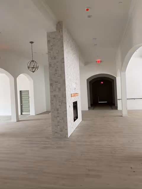 Open airy communal living area with a central tiled double-sided fireplace, arched doorways, and wood-look flooring.