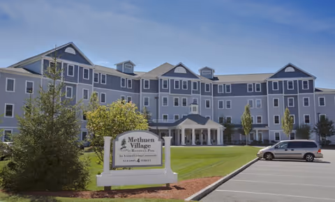 Exterior view of Methuen Village building with a sign, parking, and manicured lawn.