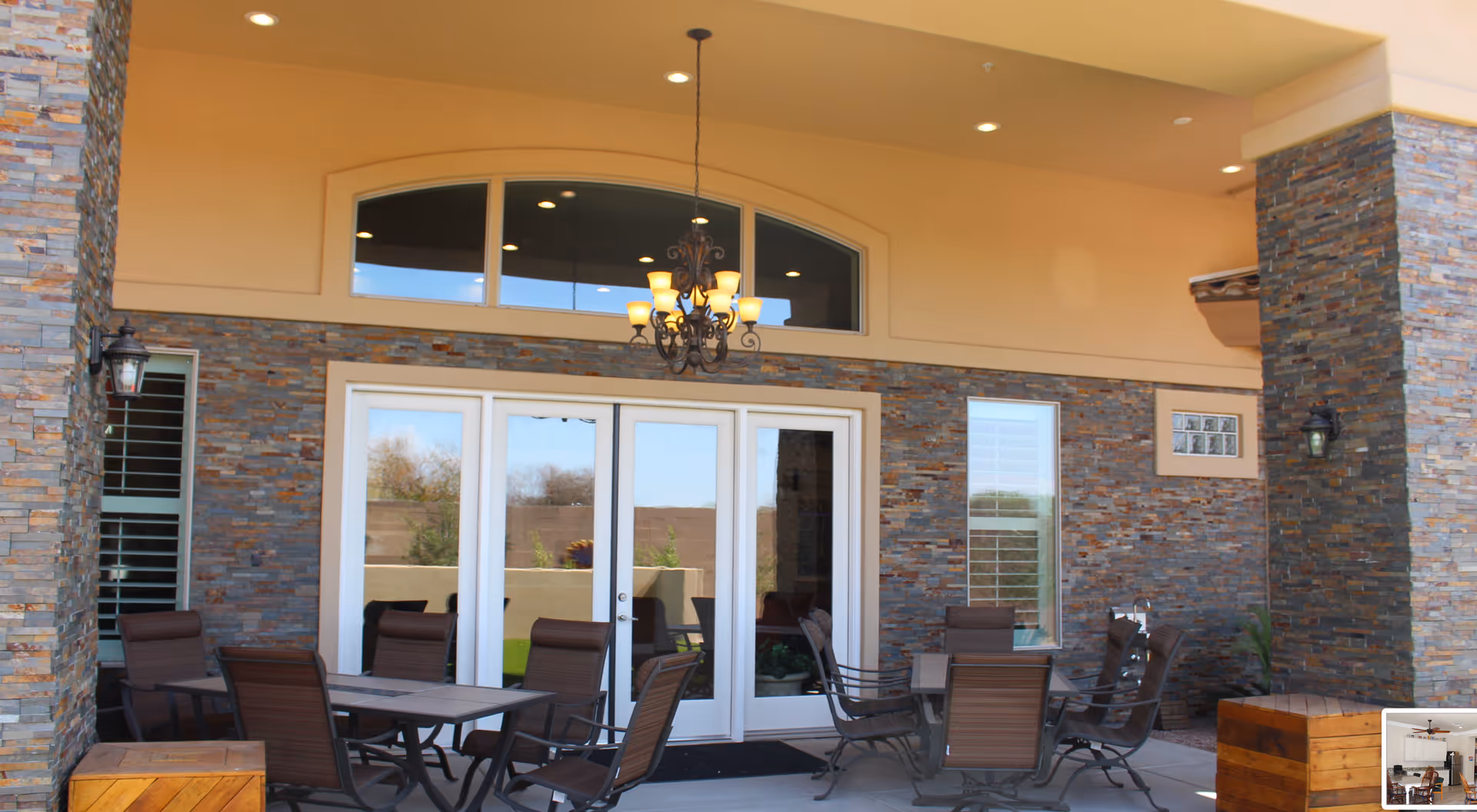 Covered outdoor patio with stone-clad walls, glass doors, a hanging chandelier, and several tables and chairs.