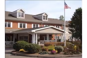 Exterior view of a two-story brick building with white trim and a covered entrance. There are bushes and landscaped plants in front, and an American flag is flying on a flagpole near the entrance.