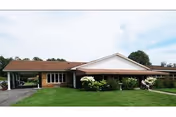 Single-story brick healthcare building with a covered entrance, striped awning, and a grassy front lawn with shrubs.